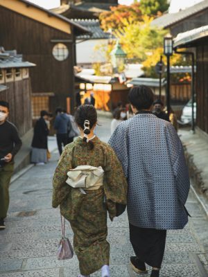 Back view faceless pedestrians wearing traditional Japanese clothed strolling on narrow paved street in sunny Asian town