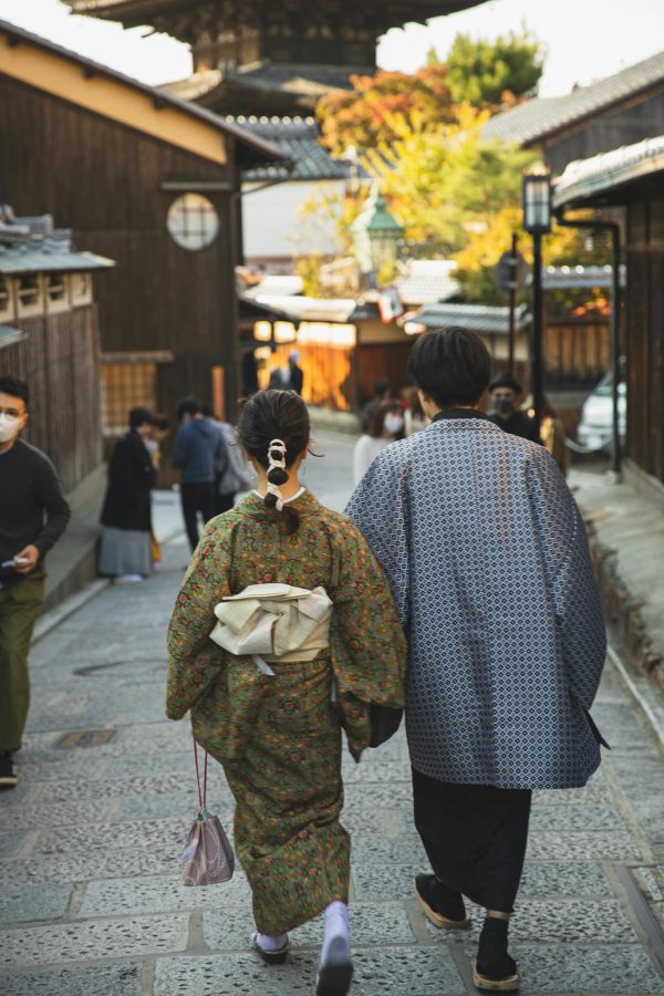 Back view faceless pedestrians wearing traditional Japanese clothed strolling on narrow paved street in sunny Asian town
