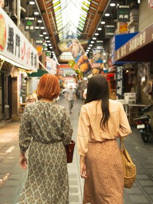 Back view of unrecognizable trendy female travelers in stylish clothes walking in traditional famous Nishiki Market in Kyoto