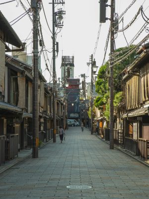 Unrecognizable people walking on narrow paved street between aged typical oriental houses on sunny day in Kyoto
